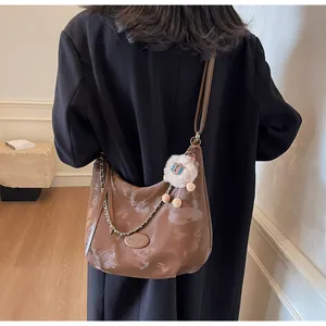 Detail of dark brown vintage hobo bag with cloud texture, metal chain and plush charm