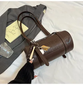 Detail der braunen Zylinder-Tasche mit Prägebuchstaben und dekorativem Baseball-Anhänger