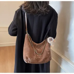 Brown semi-circle hobo bag with gold chain and bear charm shown on a black coat