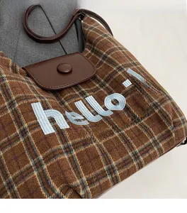 Detail of plaid tote bag with 'hello!' embroidery and brown leather snap closure flap