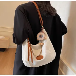 Detail of white tote bag with metal chain, brown leather strap, and plush lion charm