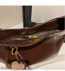 Detail of smooth gold zipper closure on dark chocolate leather tote with plush charm