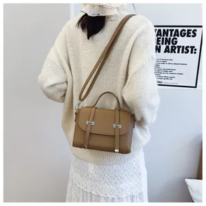 Detail of brown textured crossbody bag with silver buckles on a minimalist model
