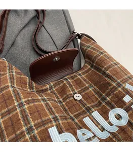 Detail of tartan crossbody bag showing magnetic snap closure and hello embroidery