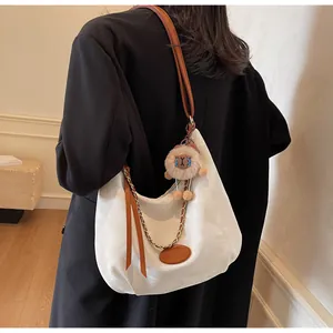 Detailed side view of white crescent tote with brown leather strap and lion charm