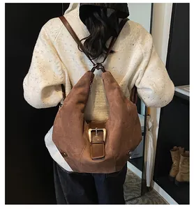 Close-up of brown suede hobo bag with large gold buckle worn on a white knit sweater