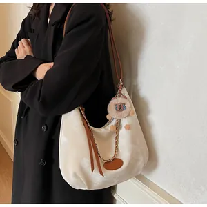 Detail of off-white tote bag with brown straps and plush charm worn by a model