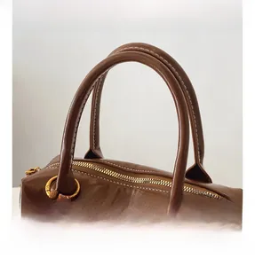 Macro detail of glossy brown leather handles with precise stitching and metal zipper