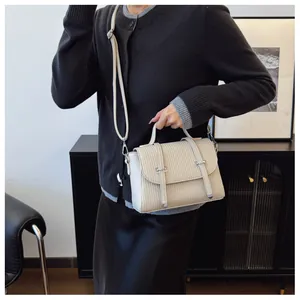 Detail of cream-colored crossbody bag featuring vertical textured patterns and shoulder strap