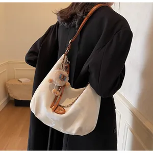 Detail of white pleated hobo bag with brown leather strap, gold chain and bear charm