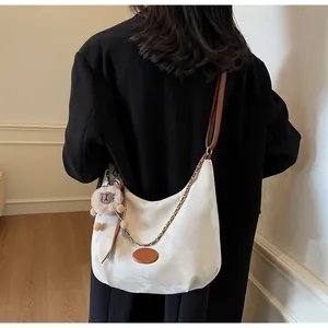 White crescent hobo bag with brown strap and plush lion charm worn on model