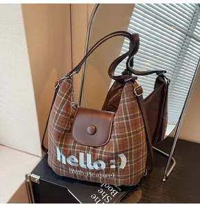 Close-up of brown plaid tote bag with leather flap and 'hello :)' embroidery detail
