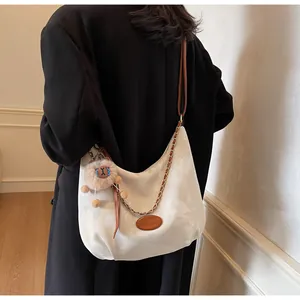 Detail of hobo crossbody bag with metal chain, brown strap and plush lion charm
