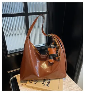 Close-up of retro brown glossy leather tote bag with a cute cartoon cat charm on a marble table
