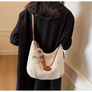 Detail of cream tote bag with brown leather straps and plush charm on a model's shoulder