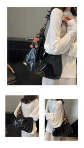 Detail of glossy black large tote bag with pleated texture and cute monkey pendant charm