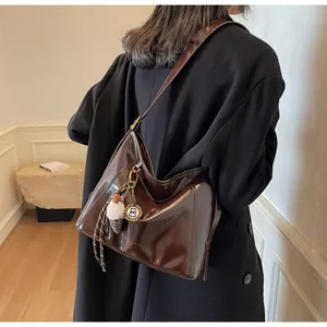 Side view of woman in black coat wearing a glossy dark brown hobo shoulder bag with charms