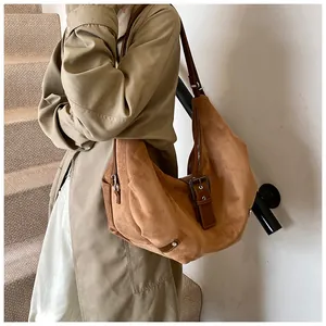 Brown suede hobo bag with retro buckle detail worn by a model in a minimal setting