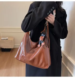 Detail of high-gloss brown patent leather tote bag with a cartoon cat charm accessory