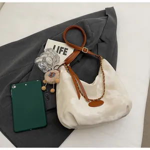 Detail of cream half-moon cloud texture bag with lion charm and golden chain