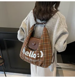 Detail of plaid tote bag featuring hello embroidery and brown leather flap closure