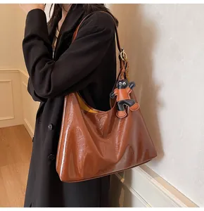 Detail of brown glossy leather tote bag with stylish charm on model shoulder