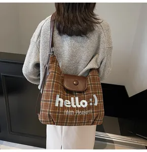 Close-up of brown plaid tote bag with 'hello' embroidery and leather shoulder strap