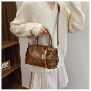Detail of a brown Boston bag with dual handles, abacus charm and adjustable shoulder strap