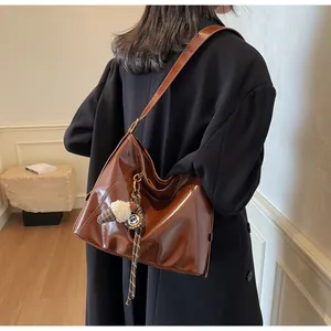 Detail view of brown glossy leather tote bag featuring plush charm and stylish silk scarf