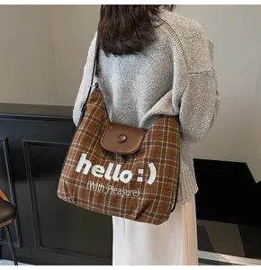 Brown plaid tote bag with leather flap and smiling face embroidery shown on shoulder