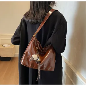 Detail of a large brown glossy tote bag with creative plush charm on a wide shoulder strap