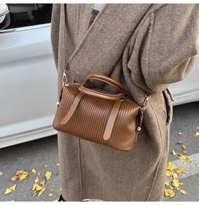 Detail of a brown pleated bucket bag with gold hardware and elegant crossbody strap