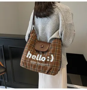 Detail of plaid tote bag with brown leather flap and hello embroidery on fabric