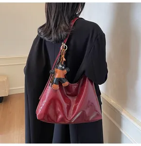 Close-up of glossy burgundy patent leather tote bag featuring a cute cat leather charm