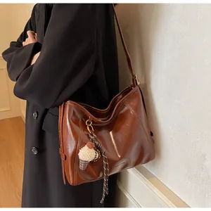 Detail of dark brown polished leather hobo bag with plush charm and ribbon accent
