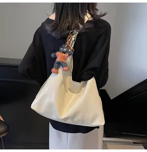 Detail of a large cream tote bag with glossy finish and cute cat pendant on a model