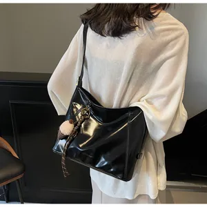 Model wearing a glossy black tote bag with a soft pompom charm and adjustable strap