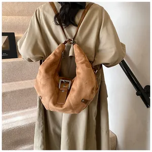 Brown faux suede crescent hobo bag shown being worn over the shoulder with a trench coat