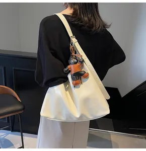 Close-up of cream-colored leather hobo bag with wide shoulder strap and animal charm