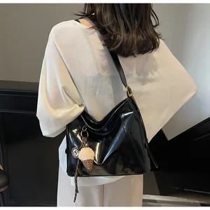 Glossy black leather tote bag shown on shoulder with minimalist decorative charm