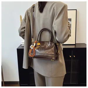 Detailed shot of dark coffee leather handbag with gold buckle and beaded charm pendant