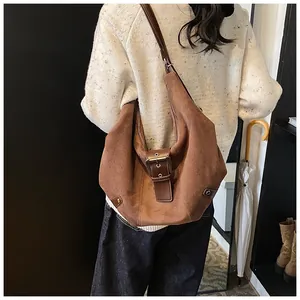 Detailed view of a brown suede hobo bag with leather buckle on a model's shoulder
