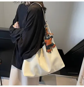 Detail of off-white leather tote bag featuring a cute black cat charm and pleated texture