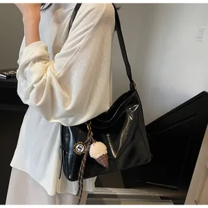 Detail of glossy black leather tote bag with ice cream charm and striped ribbon accent