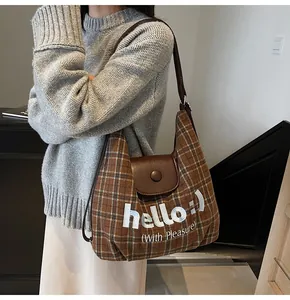 Close-up of brown plaid tote with white 'hello' embroidery and leather snap flap cover