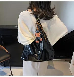 Glossy black tote bag with cute animal charm shown on a shoulder in a minimal setting