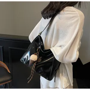 Close-up of black glossy hobo bag with a cute plush ice cream pendant on wide strap