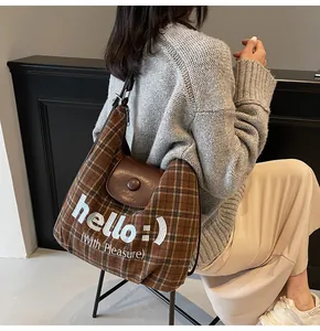 Close-up of brown plaid tote bag with leather flap and 'hello :)' embroidery detail
