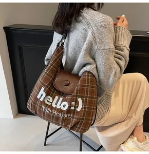 Brown plaid tote bag detail with leather flap and 'hello' graphic print decoration