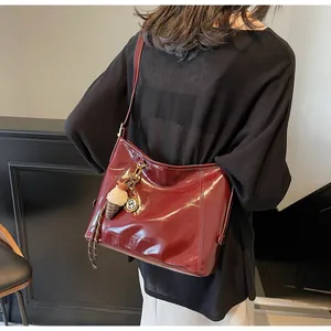 Detail view of burgundy glossy tote bag with charms shown on shoulder with light background